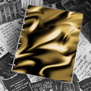 May include: A gold spiral bound notebook with a textured cover. The notebook is surrounded by black and white paper scraps with inspirational quotes and sayings. Some of the text includes "Every child is gifted", "Be full of joy", and "What Susie says of Sally says more of Susie than of Sally".