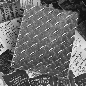 Puede incluir: Una imagen en blanco y negro de un diario encuadernado en metal con citas y refranes inspiradores en trozos de papel que lo rodean. Las citas incluyen "Estar con alguien que te haga reír cuando no te apetezca" y "Cada niño es un regalo. Simplemente desempaquetan sus paquetes en diferentes momentos."