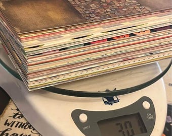 May include: A stack of patterned paper squares, featuring vintage designs and textures, rests on a white digital kitchen scale. The scale displays a weight of 30.1, indicating the weight of the paper. The paper has a variety of colors and patterns.