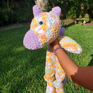May include: A crocheted unicorn plush toy with a rainbow swirl pattern in shades of purple, pink, yellow, and white. The unicorn has a purple horn and a blue eye.