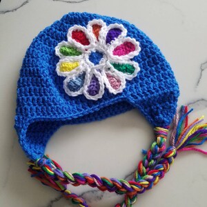 May include: A blue crocheted hat with a colorful flower design and a long, braided tassel.