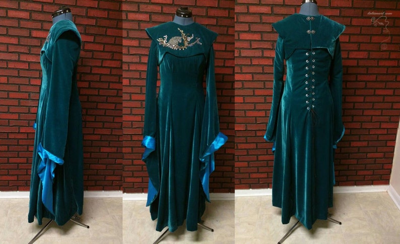 May include: Teal velvet gown with long sleeves and a flared skirt. The dress features a high collar and a decorative embellishment on the bodice. The sleeves have blue satin cuffs. The back of the dress has a corset-style closure. The dress is displayed on a mannequin.