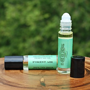 May include: Two 10 ml roll-on bottles of Forest Air aromatherapy perfume oil. The bottles are clear glass with black caps and a green label that says "Aromatherapy's Perfume Oil Forest Air" and "The Herb & Soap Co."