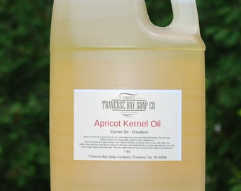 May include: A white plastic jug with a green lid filled with yellow apricot kernel oil. The label reads "Traverse Bay Soap Co. Apricot Kernel Oil Carrier Oil - Emollient 7 lbs Traverse Bay Soap Company, Traverse City, MI 49686".