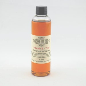 May include: A clear glass bottle with a black cap filled with a light brown liquid. The label reads "Traverse Bay Soap Co. Vitamin E - T-50 Tocopherol 100% pure oil 4 oz wt Traverse Bay Soap Company, Traverse City, MI".