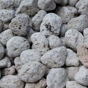 May include: A close-up of a basket filled with light gray pumice stones. The stones are rough and porous, with a variety of shapes and sizes.
