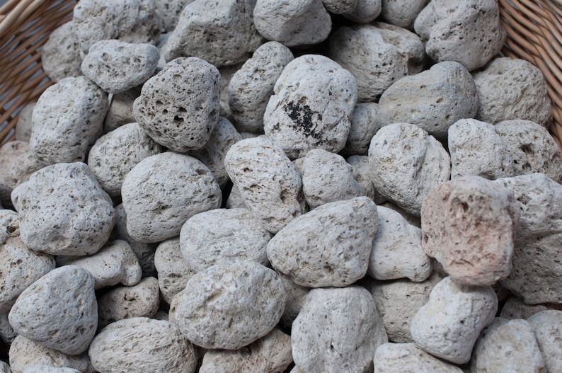 May include: A close-up of a basket filled with light gray pumice stones. The stones are rough and porous, with a variety of shapes and sizes.