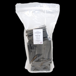 May include: A clear plastic bag filled with black pine tar ends and pieces. The bag has a label that reads "Pine Tar Ends & Pieces".