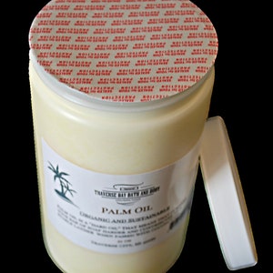 May include: A white jar with a red and white tamper-evident seal on the lid. The jar contains a pale yellow substance and has a label that reads "Traverse Bay Bath and Body" and "Palm Oil Organic and Sustainable".