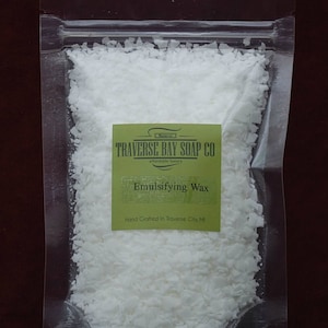May include: A clear plastic bag filled with white emulsifying wax flakes. The bag has a label that reads "Traverse Bay Soap Co. affordable luxury" and "Emulsifying Wax". The label also states "Hand Crafted in Traverse City, MI".