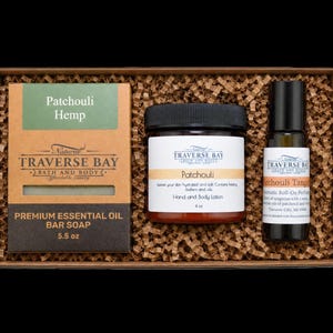 May include: A gift box containing a 5.5 oz bar of Patchouli Hemp soap in a brown box, a 4 oz jar of Patchouli hand and body lotion with a black lid, and a bottle of Patchouli Tangerine roll-on perfume, all nestled in brown shredded paper.