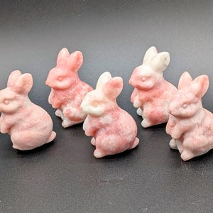 May include: Five carved stone bunny figurines in shades of pink and white. The bunnies are in a sitting position with their ears upright. The stone has a marbled appearance, and the bunnies are smooth and detailed.