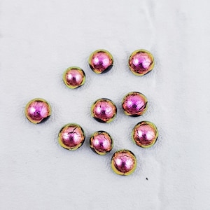 May include: Ten iridescent glass beads with a pink and green colour scheme. The beads have a cracked or textured surface.