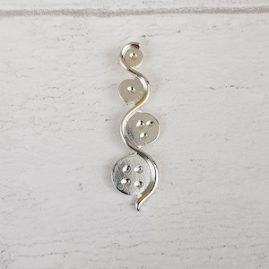 Könnte beinhalten: Silberner Anhänger mit einer Reihe verbundener Kreise, jeder mit einem erhabenen Punktmuster.