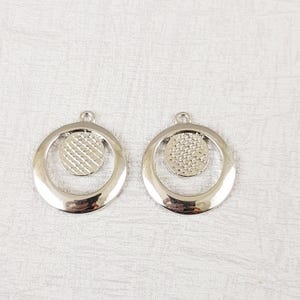May include: Two silver-toned metal earring charms with a circle design. Each charm features a smaller circle with a textured surface inside a larger circle.