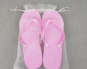 May include: A pair of pink flip-flops in a clear plastic bag. The flip-flops are made of a soft, rubbery material and have a simple design.