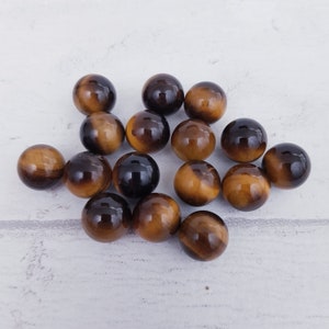 May include: A collection of 15 smooth, round tiger's eye stones in shades of brown and gold.