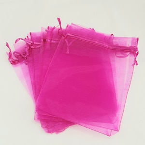 Op de afbeelding: Een stapel roze organza cadeauzakjes met trekkoord. De zakjes zijn gemaakt van transparante stof en zijn perfect voor kleine cadeautjes of attenties.