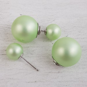 May include: A pair of green pearl earrings with a double-sided design. The earrings are made of a smooth, shiny material and have a silver-toned post.