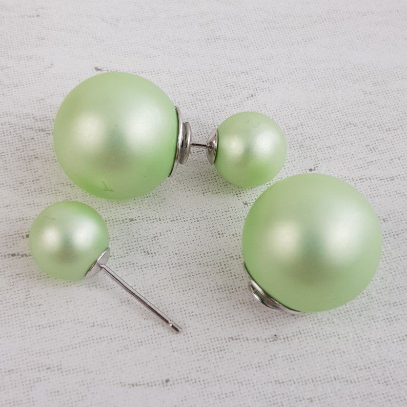 May include: A pair of green pearl earrings with a double-sided design. The earrings are made of a smooth, shiny material and have a silver-toned post.