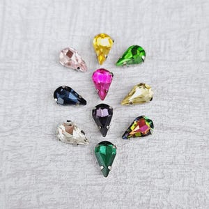 May include: Assortment of teardrop shaped rhinestones in various colours, including pink, green, black, purple, and clear.