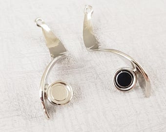 Puede incluir: Dos hallazgos de pendientes de plata con un diseño curvo. Un hallazgo tiene un círculo negro en el centro y el otro tiene un círculo plateado en el centro.