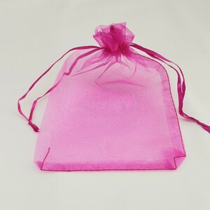 May include: A pink sheer organza gift bag with a drawstring closure. The bag is made of a delicate, translucent fabric and is perfect for small gifts or favors.