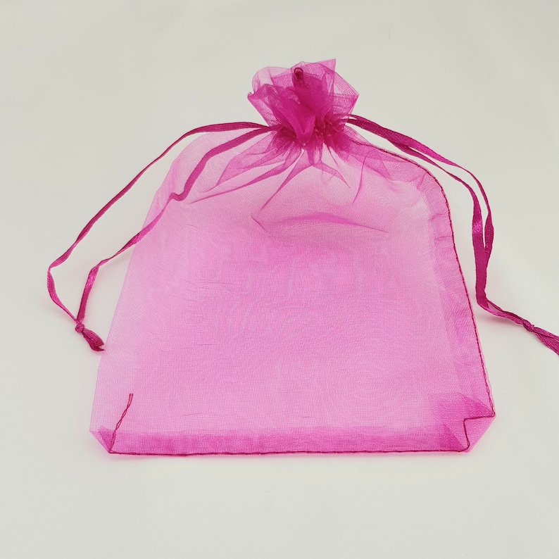 May include: A pink sheer organza gift bag with a drawstring closure. The bag is made of a delicate, translucent fabric and is perfect for small gifts or favors.