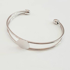 May include: Silver double-layered bangle bracelet with a round, blank, silver charm.