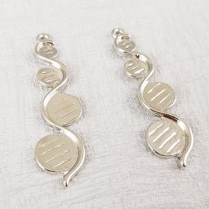 May include: Two silver-toned metal charms with a spiral design and three round, textured discs. The charms are approximately 5 cm long.