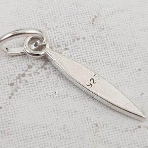 May include: Silver charm with a pointed oval shape and a loop at the top. The charm is marked with "925" on the back.