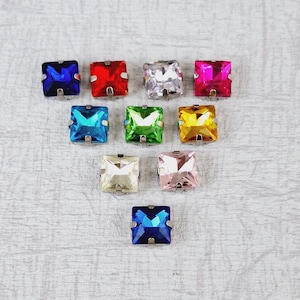 Può includere: Assortimento di dieci strass quadrati con montature argentate. Gli strass sono di vari colori, tra cui blu, rosso, bianco, rosa, verde e giallo.