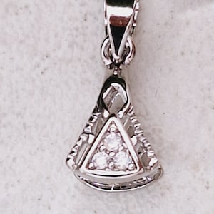 Puede incluir: Un colgante de plata con un diseño triangular y tres pequeñas piedras transparentes.