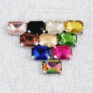 May include: Assortment of 10 rectangular shaped rhinestones with silver settings. The rhinestones are in various colors including pink, black, clear, yellow, green, brown, blue, red, and iridescent.