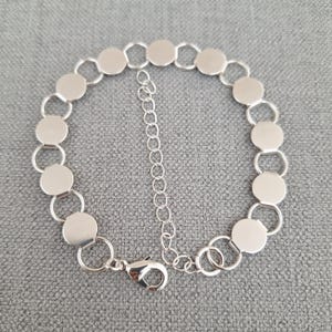 Op de afbeelding: Een zilveren kettingarmband met een reeks ronde, platte schakels. De armband heeft een karabijn sluiting.