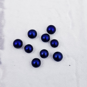 Puede incluir: Nueve canicas redondas de color azul oscuro sobre una superficie blanca.