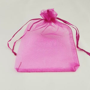 May include: A pink sheer organza drawstring bag. The bag is made of a delicate, translucent fabric and has a gathered top with a drawstring closure.