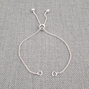 May include: A silver adjustable bracelet with a sliding clasp. The bracelet is made of a delicate chain.