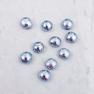 May include: Ten silver-colored, round, foil-wrapped candies on a white surface. The candies are arranged in a heart shape.