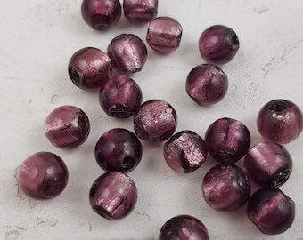 Op de afbeelding: Een verzameling van 20 paarse glazen kralen met een metallic glans. De kralen zijn rond en hebben een licht onregelmatige vorm. Ze zijn perfect voor het maken van sieraden of andere knutselprojecten.