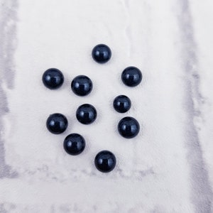 Op de afbeelding: Tien donkerblauwe ronde kralen op een wit oppervlak.