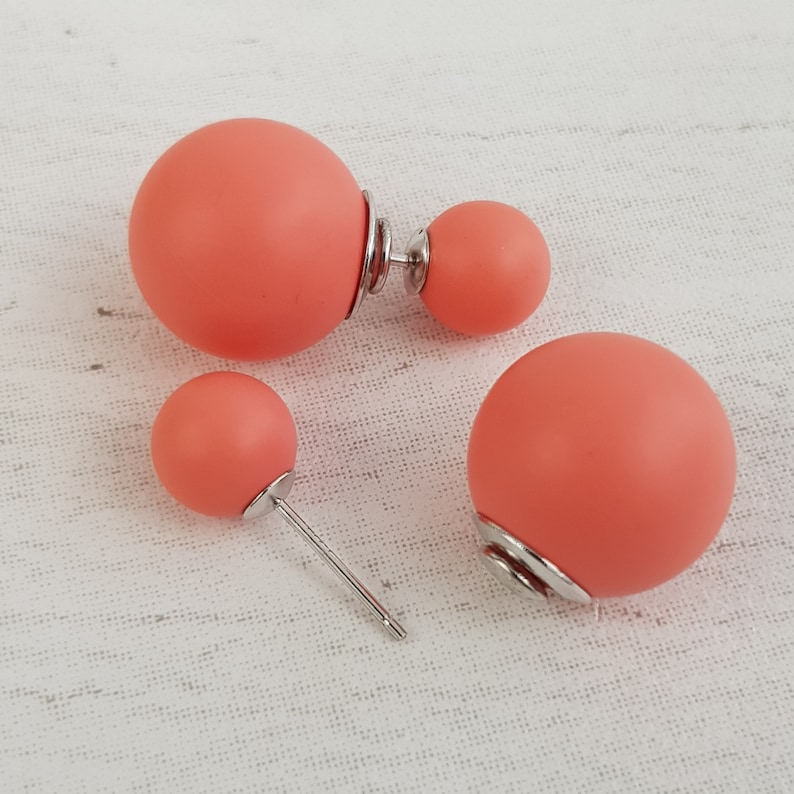 May include: A set of three coral-colored double-sided stud earrings. The earrings are made of a smooth, matte material and have a simple, modern design.