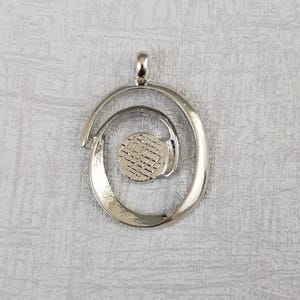 May include: Silver pendant featuring a spiral design with a small round cutout in the centre.