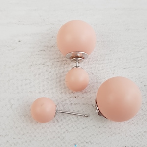 May include: A pair of peach-colored double-sided stud earrings. The earrings have a larger ball on one side and a smaller ball on the other side.