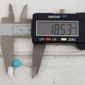 May include: A blue bead with a silver pin is measured with a digital caliper. The caliper reads 18.53 mm.