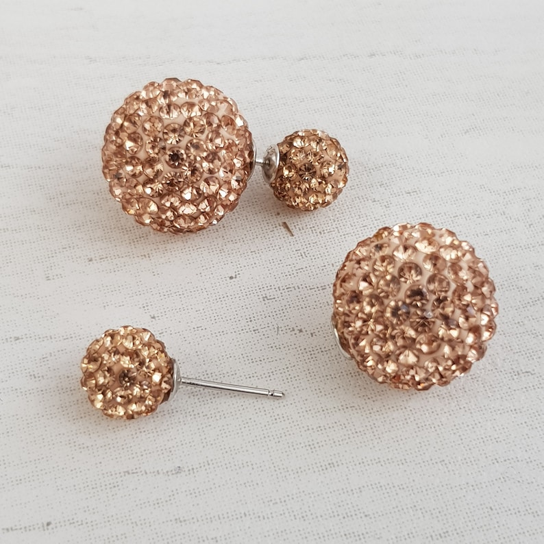 May include: A pair of gold tone double-sided earrings with a round, sparkly design. Each earring has two round, sparkly balls.