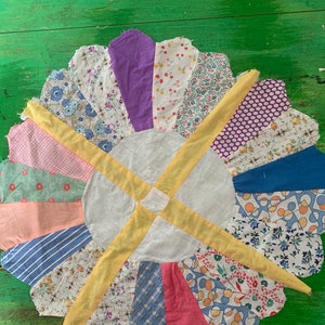 May include: A circular patchwork quilt with a white center and yellow seams. The quilt is made up of various floral and geometric patterned fabrics in shades of pink, blue, purple, and green.