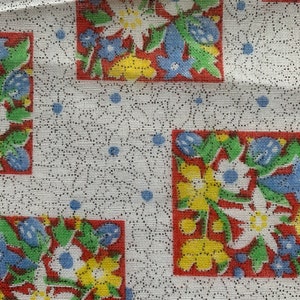 May include: White fabric with a repeating pattern of red, yellow, blue, and green floral squares. The background is a white fabric with a subtle black dot pattern.