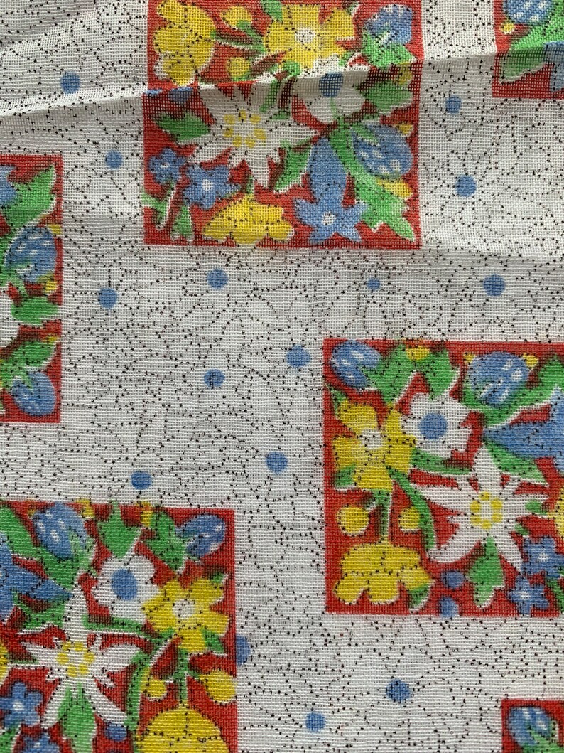 May include: White fabric with a repeating pattern of red, yellow, blue, and green floral squares. The background is a white fabric with a subtle black dot pattern.