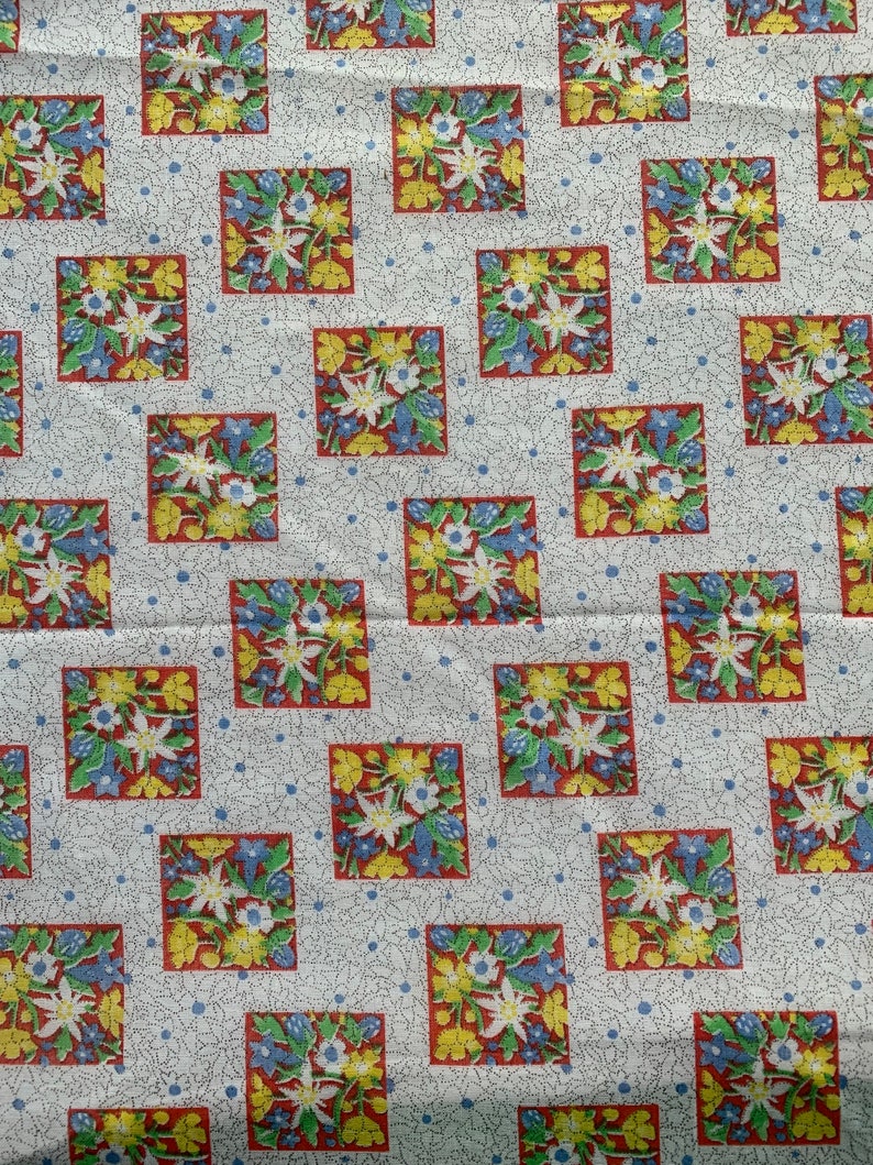 May include: White fabric with a repeating pattern of red, yellow, and blue flowers in squares. The background has a subtle blue and white dotted pattern.